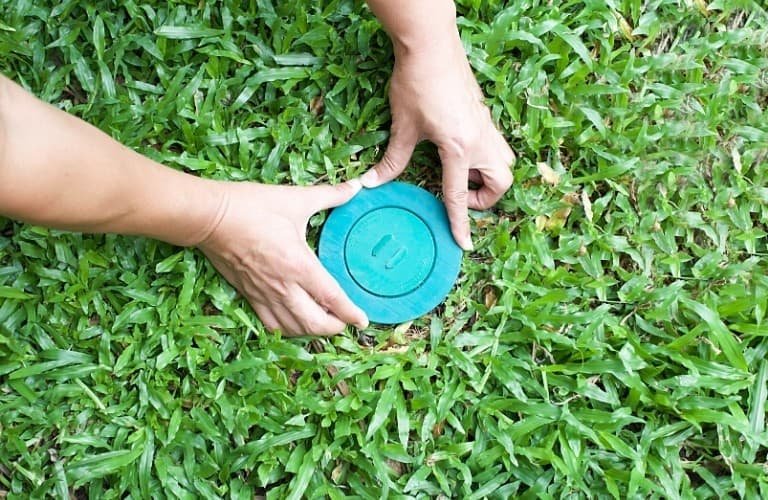 A person placing a termite bait station into the lawn.
